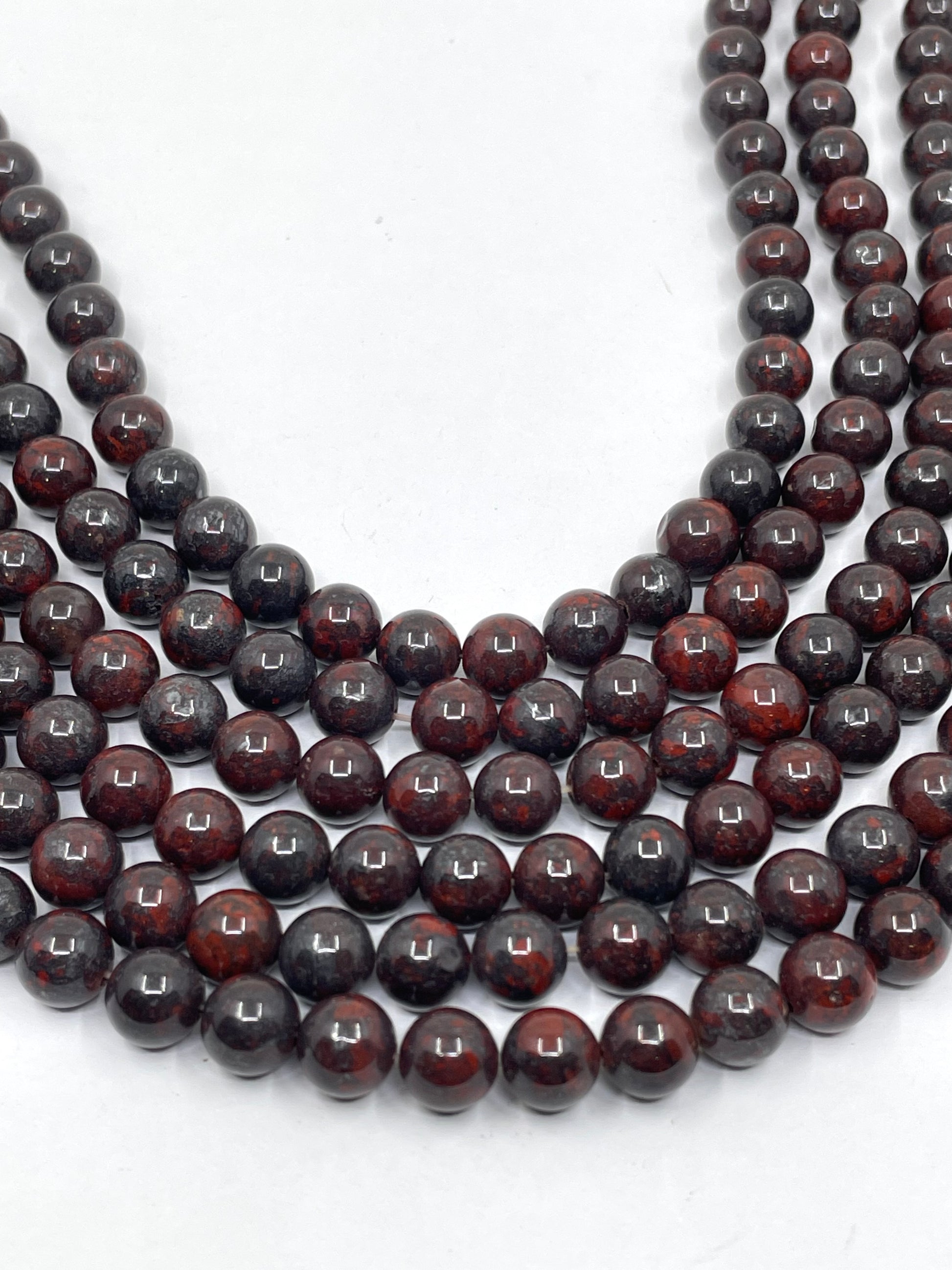 Multiple strands of polished dark reddish-brown and black round brecciated jasper beads arranged in a U-shape on a plain white background.