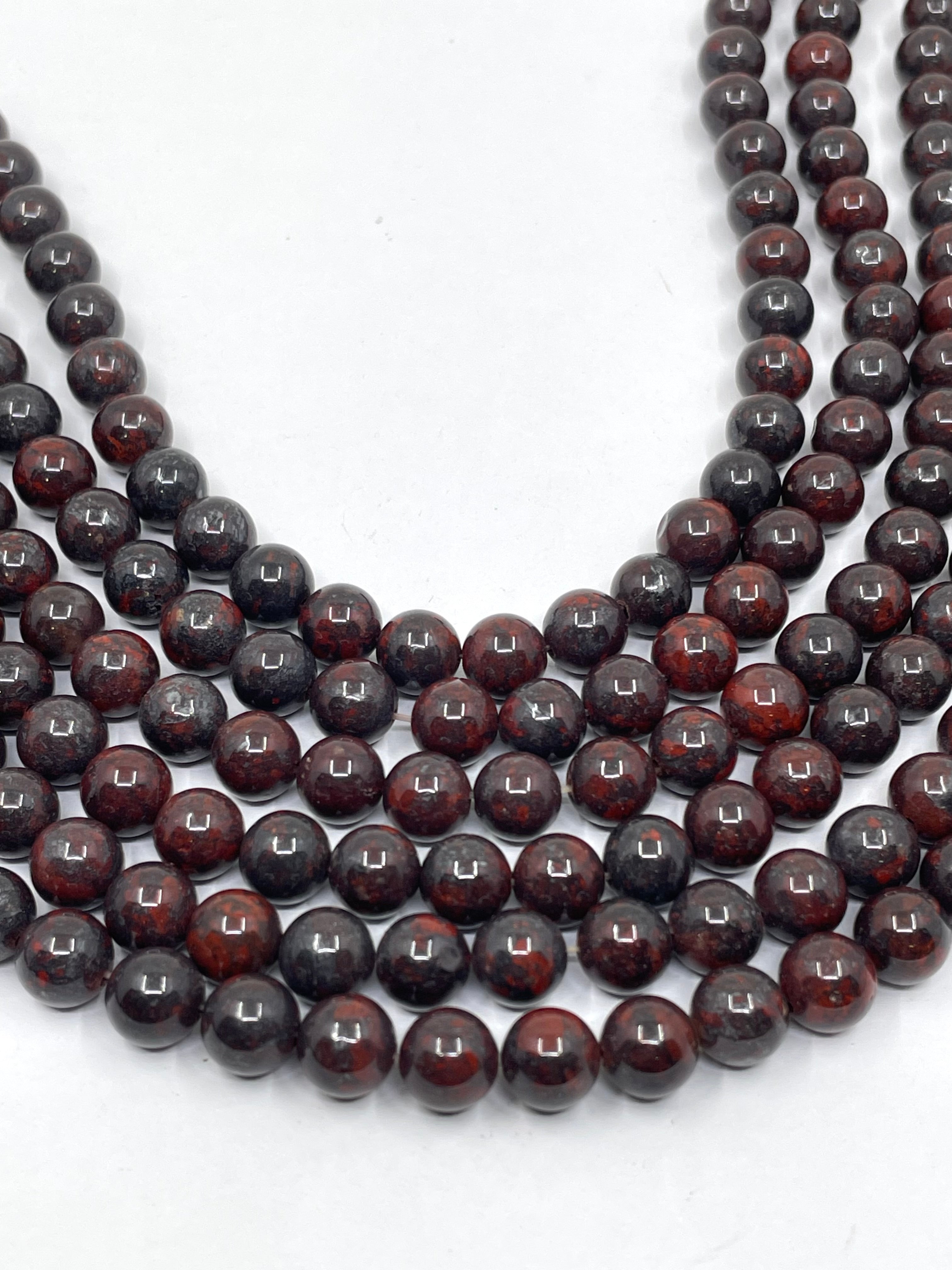 Multiple strands of polished dark reddish-brown and black round brecciated jasper beads arranged in a U-shape on a plain white background.