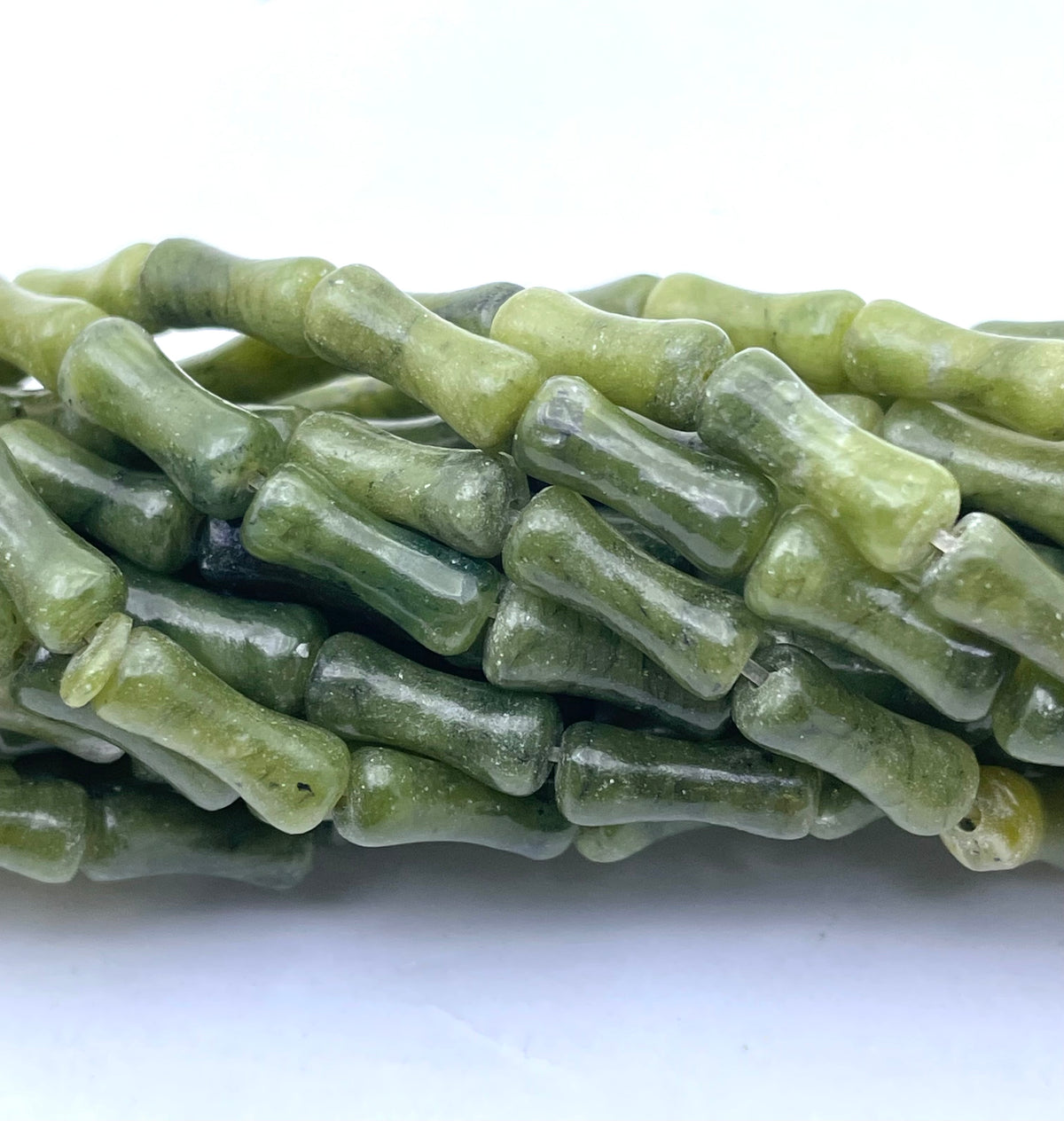 A close-up of olive green stone nephrite jade beads with a unique knotted or ribbed texture, arranged in a bundle on a plain white background.