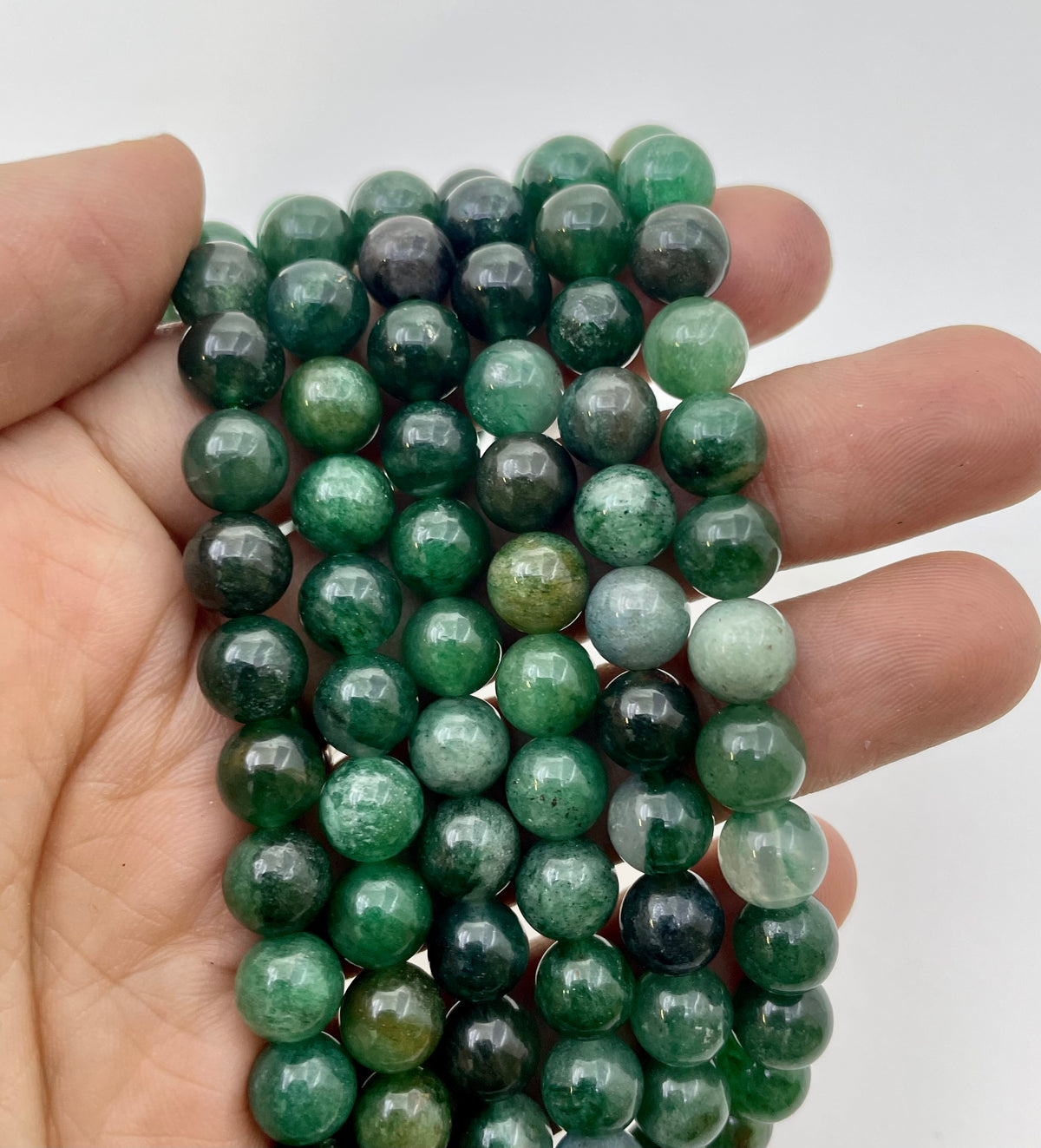 A hand holding a strand of green lepidolite gemstone beads, showing their polished round shapes and natural green variations against a plain white background.