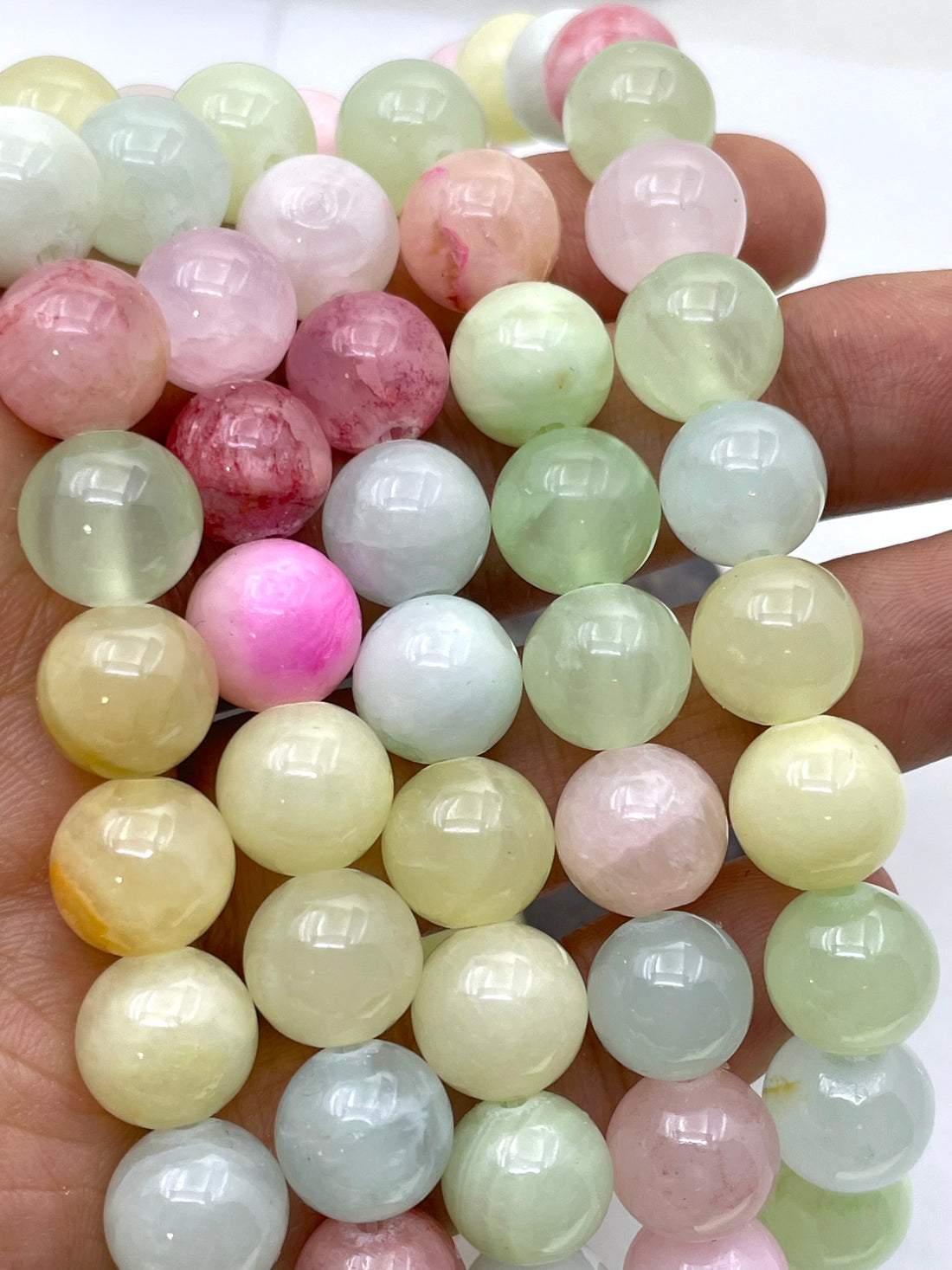 A close-up of a hand holding a strand of polished round jade gemstone beads in pastel colors, including pink, green, yellow, blue, and white.
