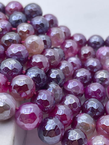 Close-up of faceted round pink agate gemstone beads in shades of pink, purple, and lavender, arranged on a light surface.