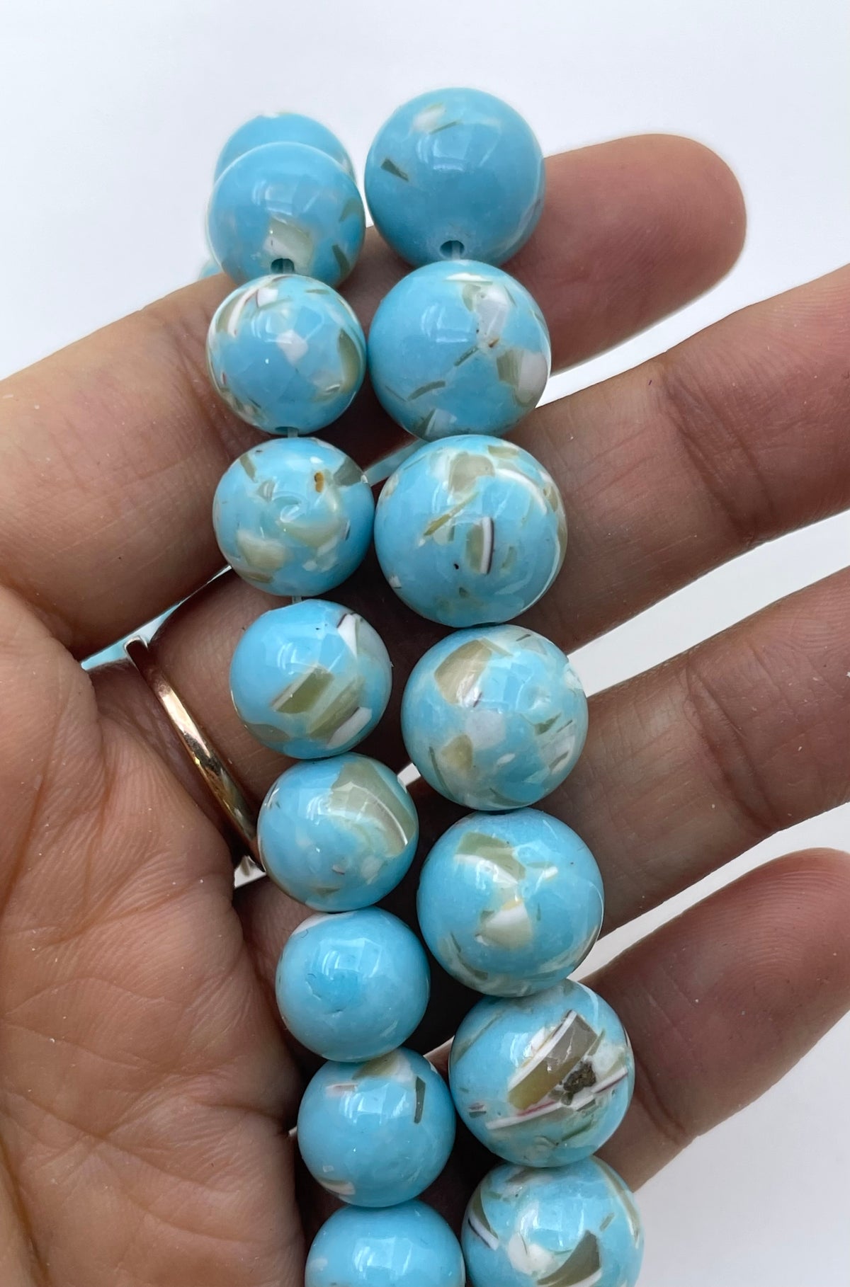 A hand holding a strand of round turquoise-blue mop beads with white marbled inclusions, photographed against a plain white background.