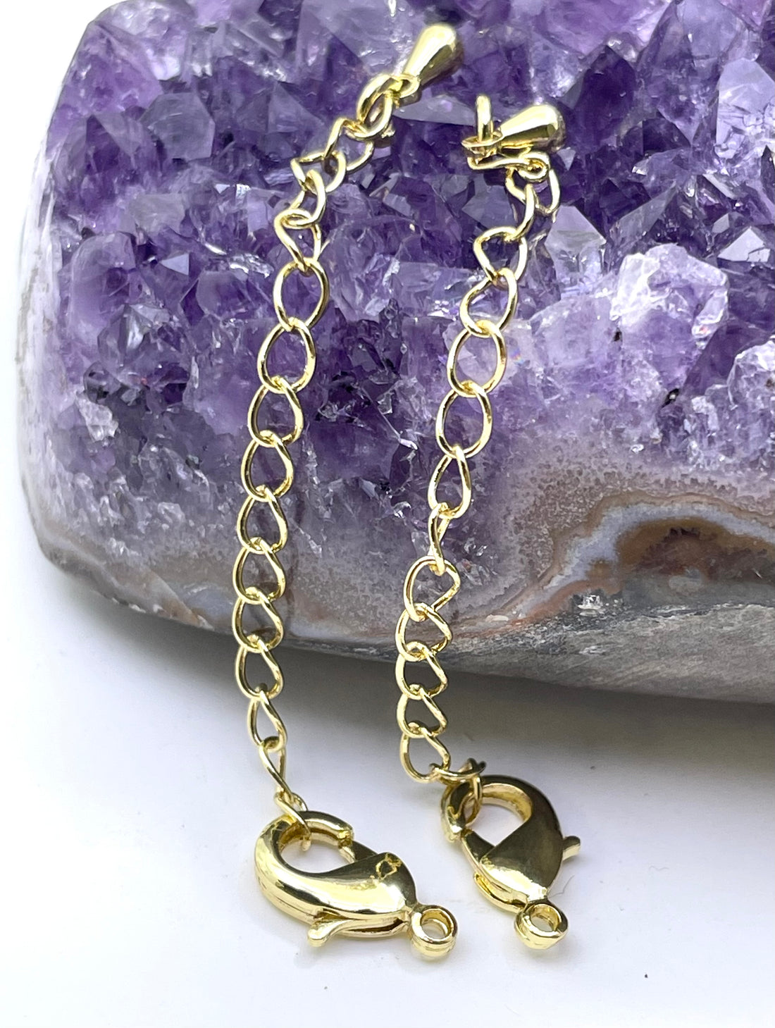 Two gold lobster claw chain extender links with spring rings, displayed on a dark wooden block against a white background.