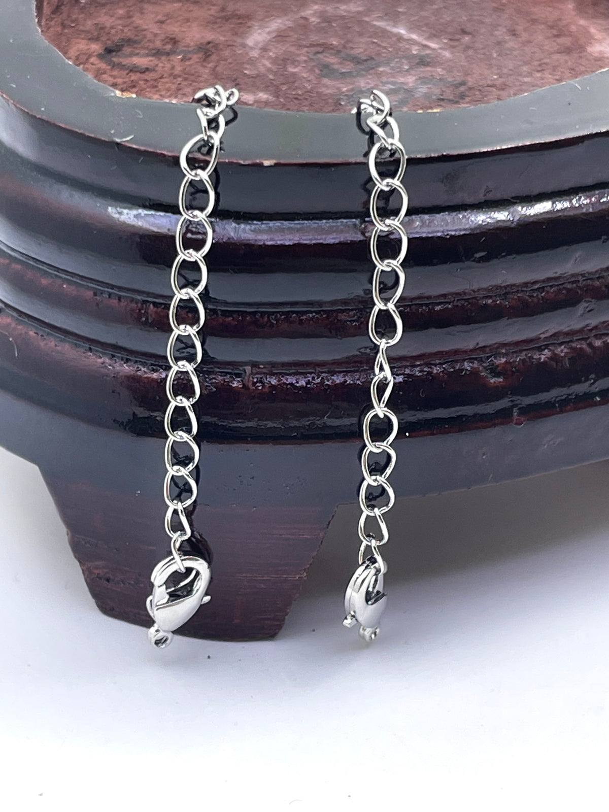 A pair of silver extension lock with elongated link chains displayed against a dark wooden stand on a white surface.