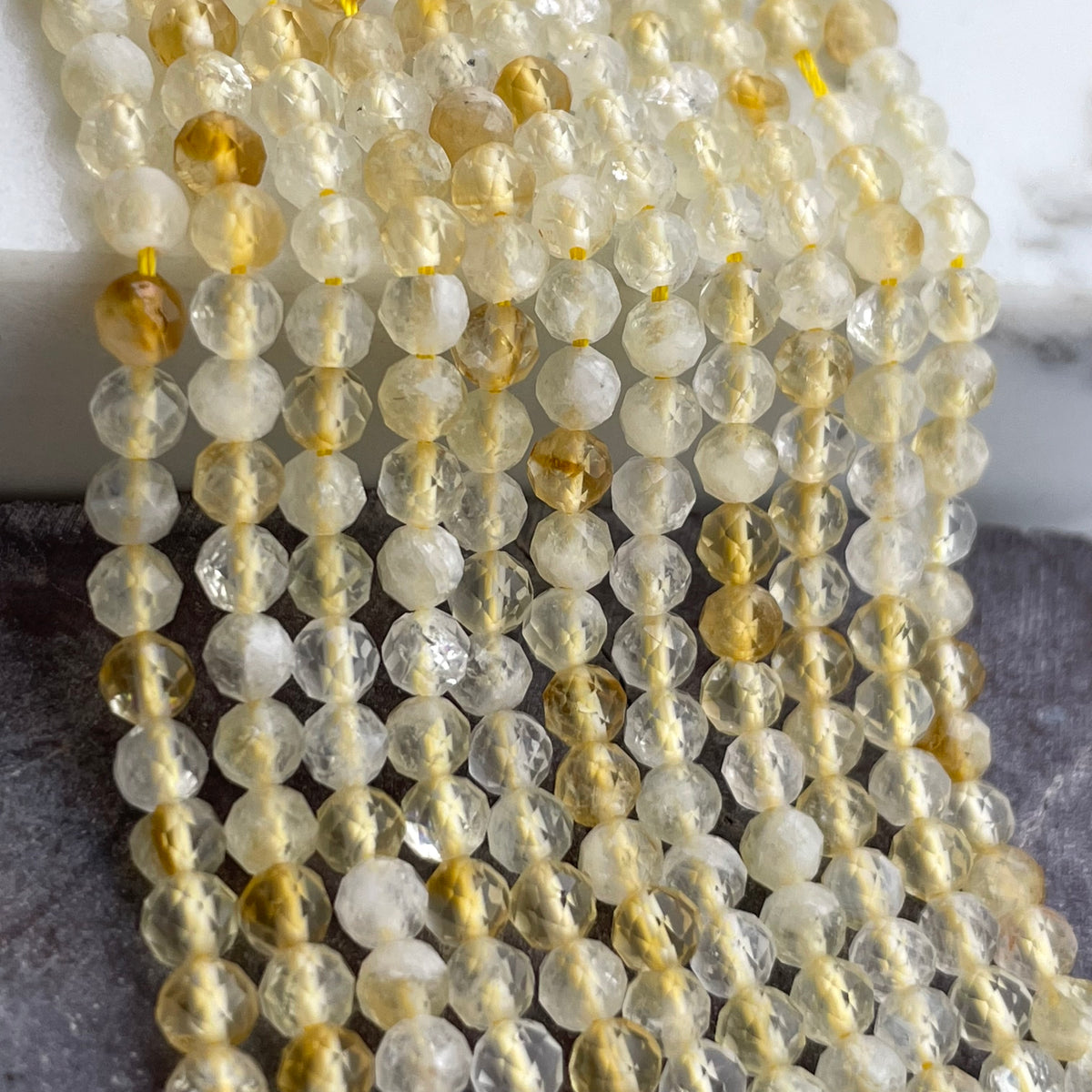 Faceted round citrine gemstone beads strung in multiple strands, showing a mix of milky white, translucent clear, and warm golden-brown tones.
