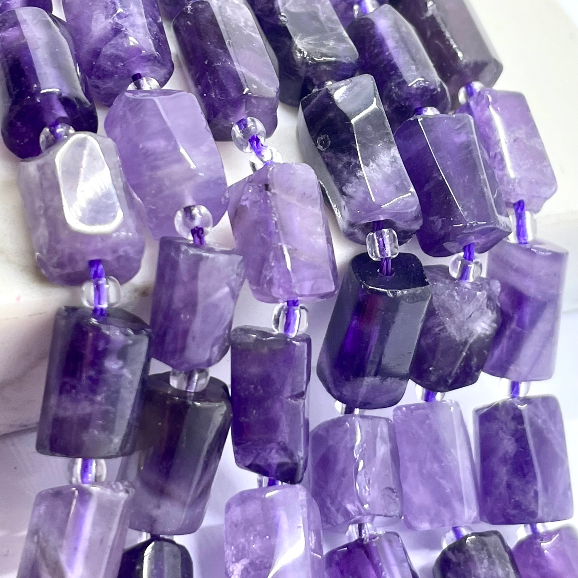 Purple amethyst gemstone beads with a faceted, polished rectangular shape, strung on silver wire with small clear spacer beads.