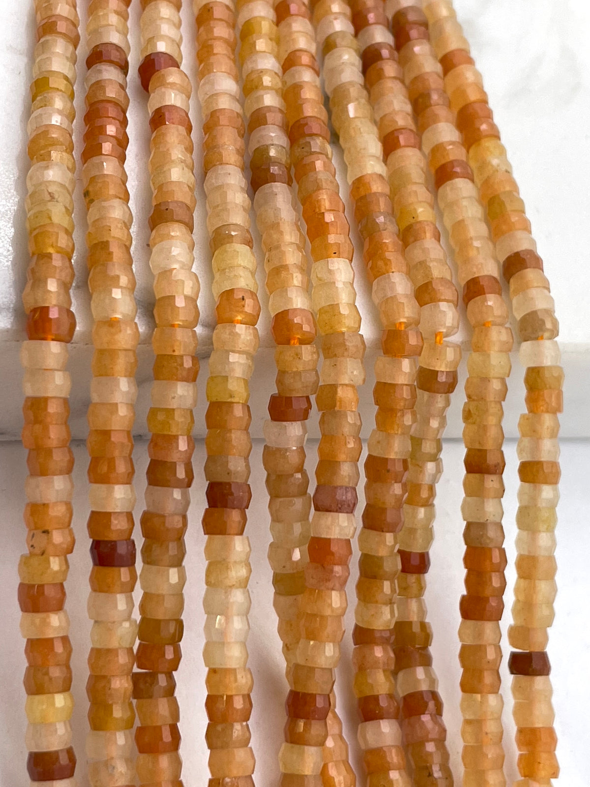 Faceted red aventurine gemstone beads in warm earthy tones of orange, brown, beige, and cream, arranged in vertical strands.