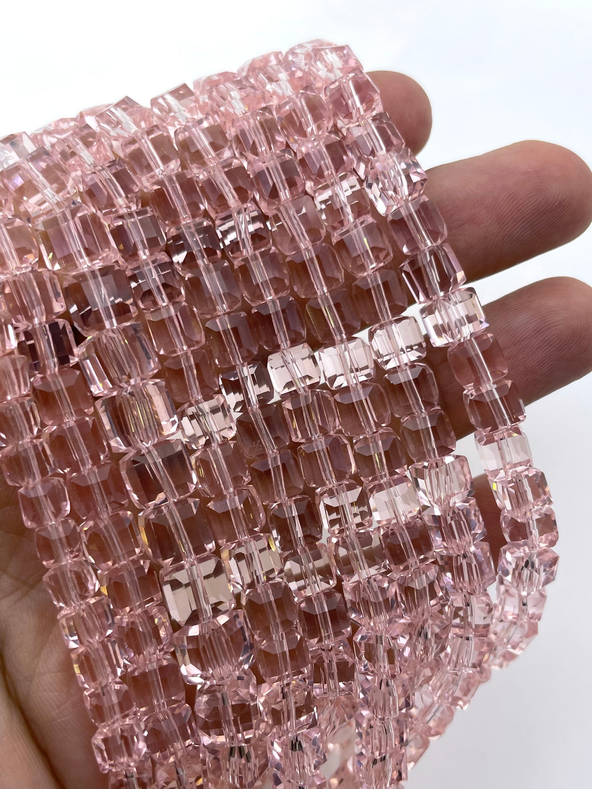 A close-up of a hand holding a bundle of faceted pink cube glass beads on a white background.