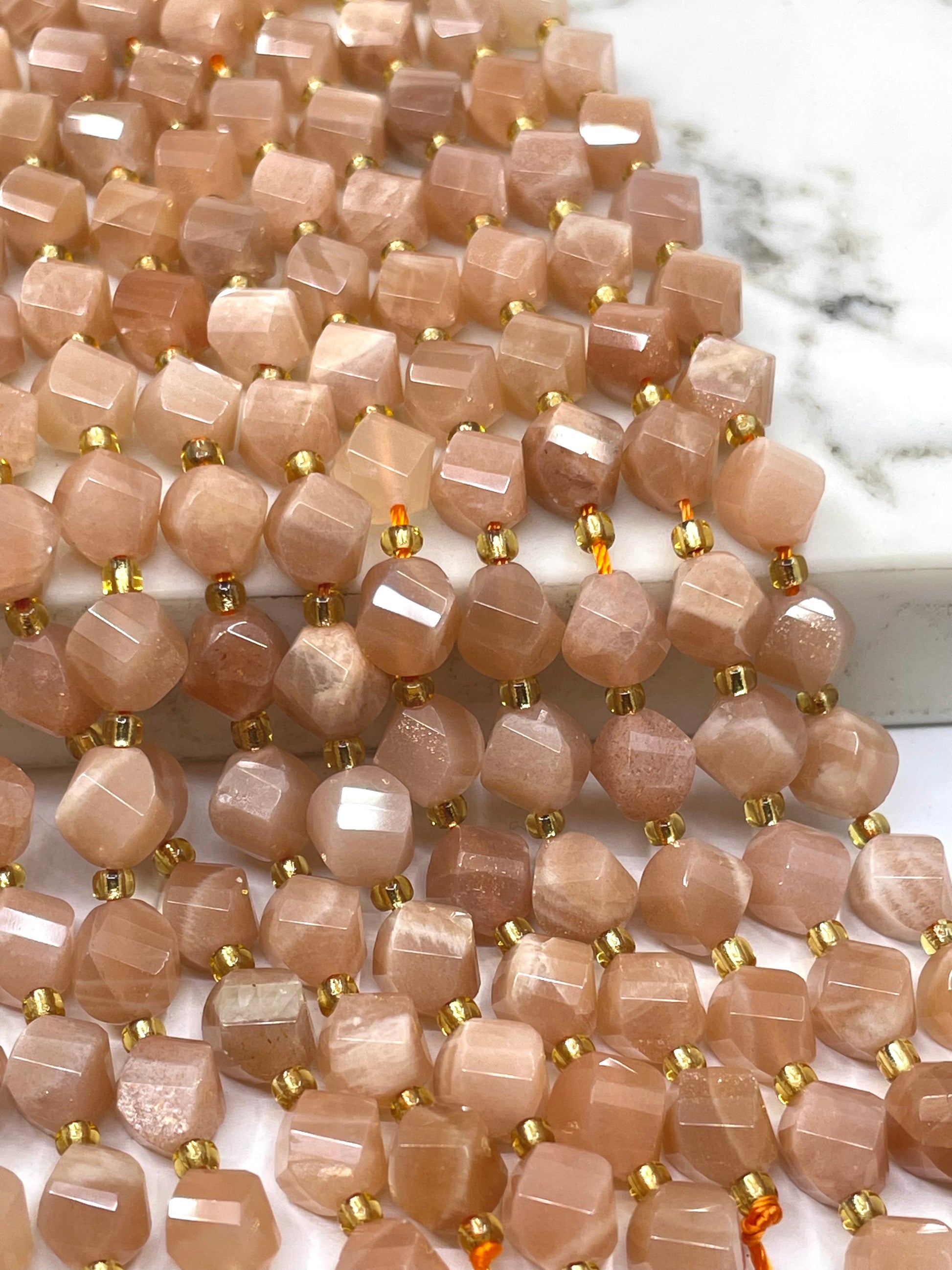 Faceted sunstone bead strands with small gold spacer beads, displayed on a white marble surface.