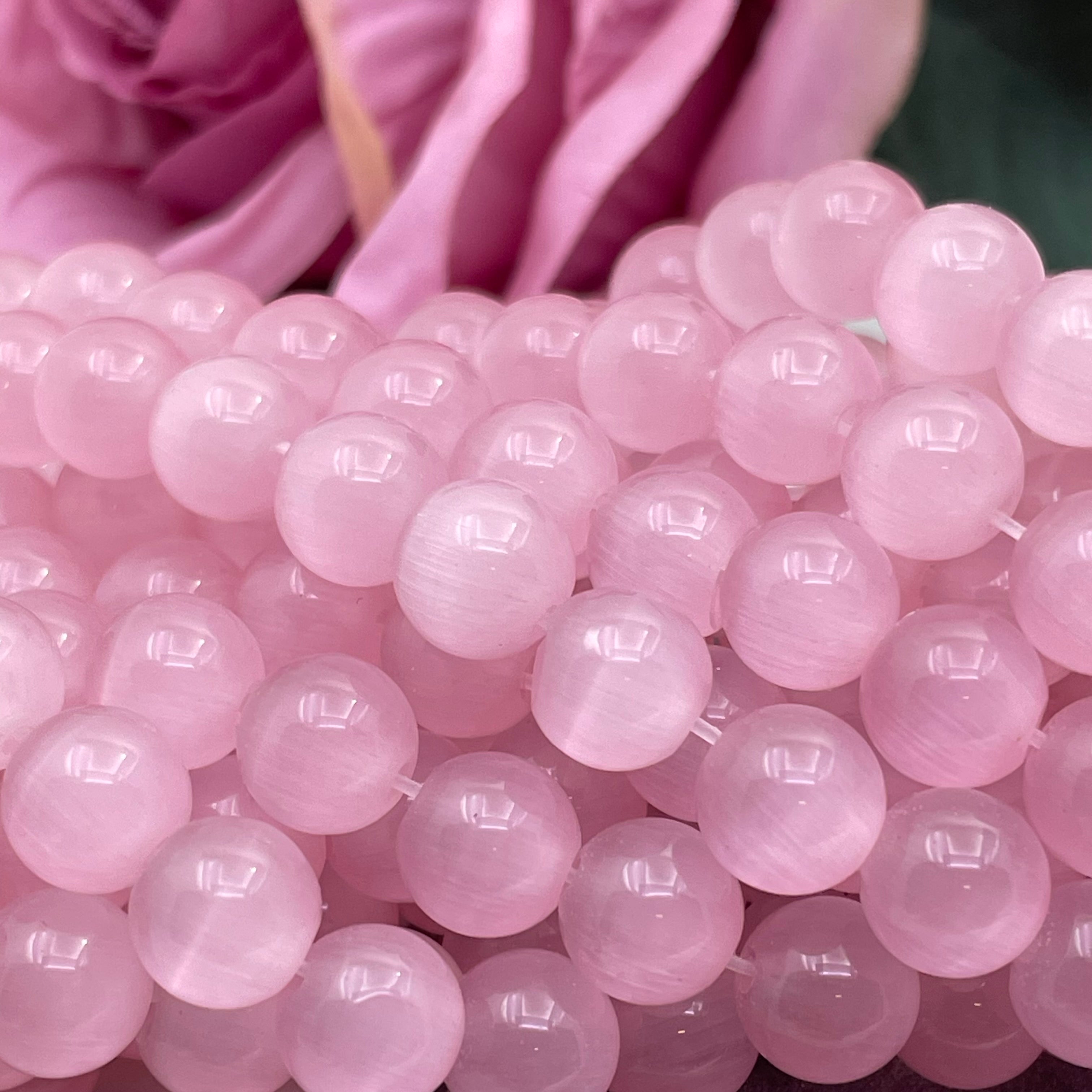 A close-up of glossy pink cats eye translucent round beads, with soft pink fabric in the background.