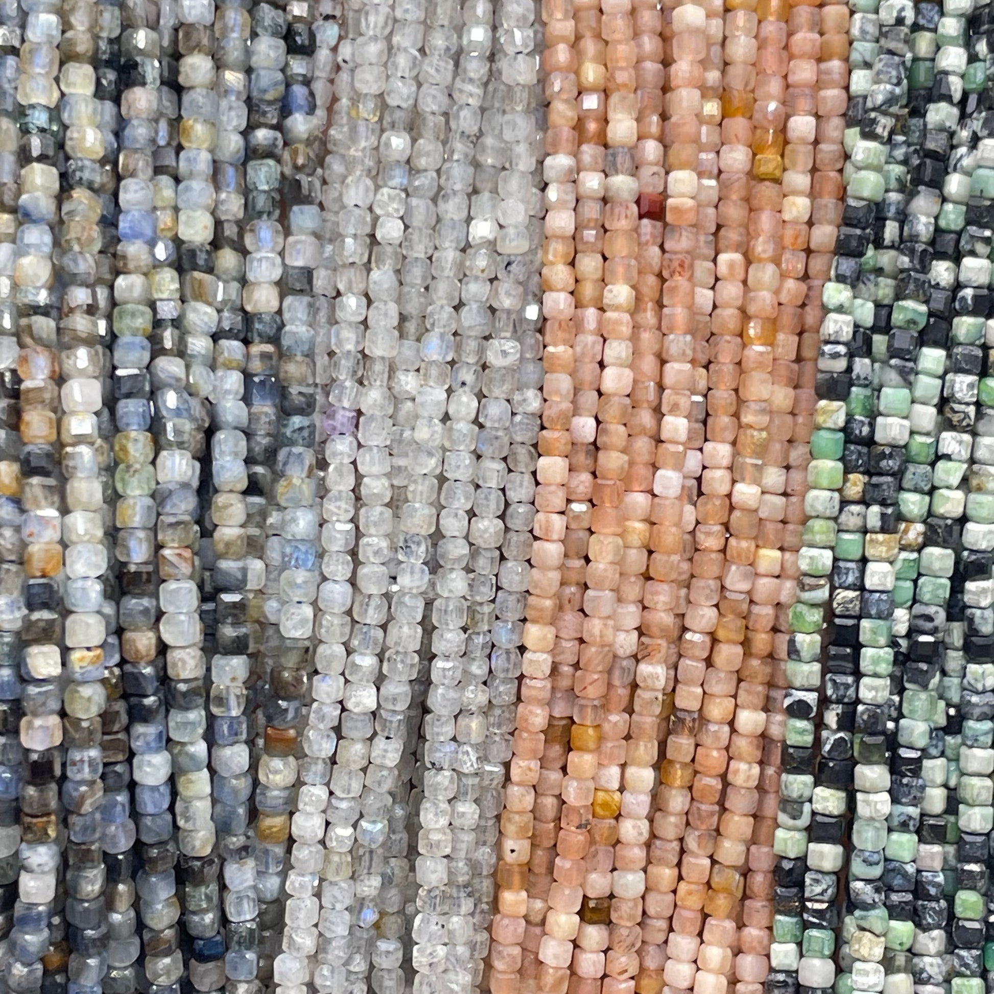 Kyanite, labradorite, peach moonstone, variscite 2mm cube faceted beads displayed from left to right in order.