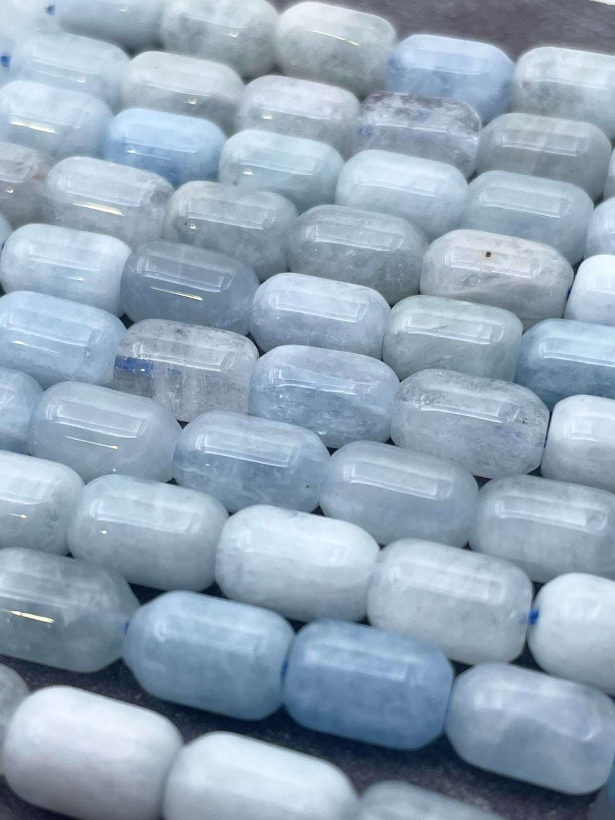Close-up of light blue and white translucent rectangular aquamarine beads with rounded edges, arranged closely together.