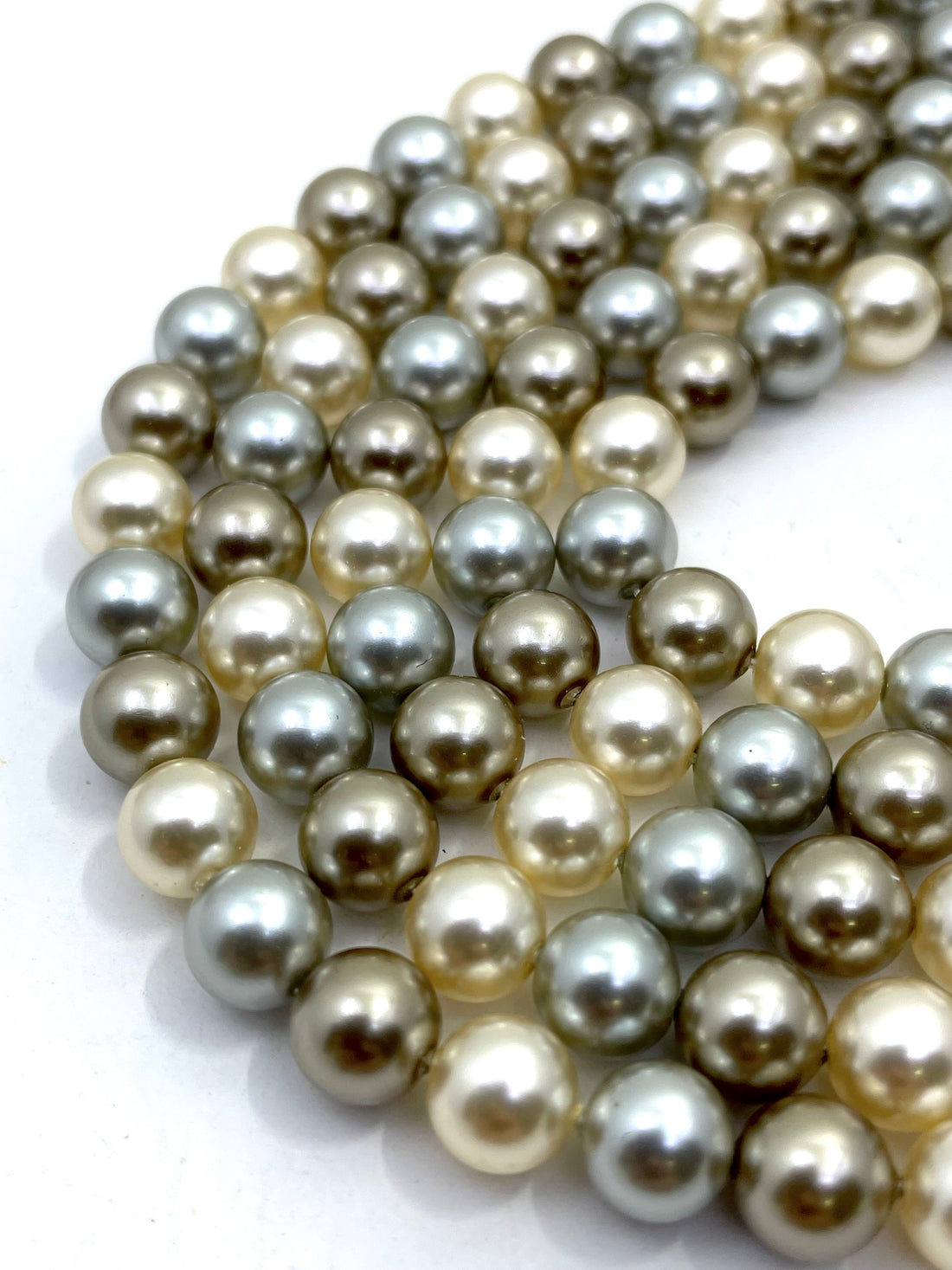 Curved strands of shell pearl beads in a mix of champagne beige, soft gray, and olive green on a white background.
