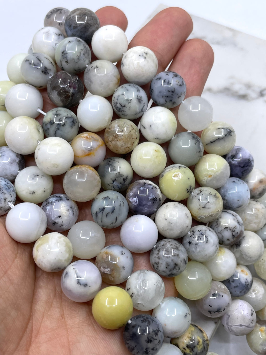 Multiple strands of polished round dendritic opal beads in a marbled pattern of white, gray, beige, brown, and black, arranged on a plain white background.