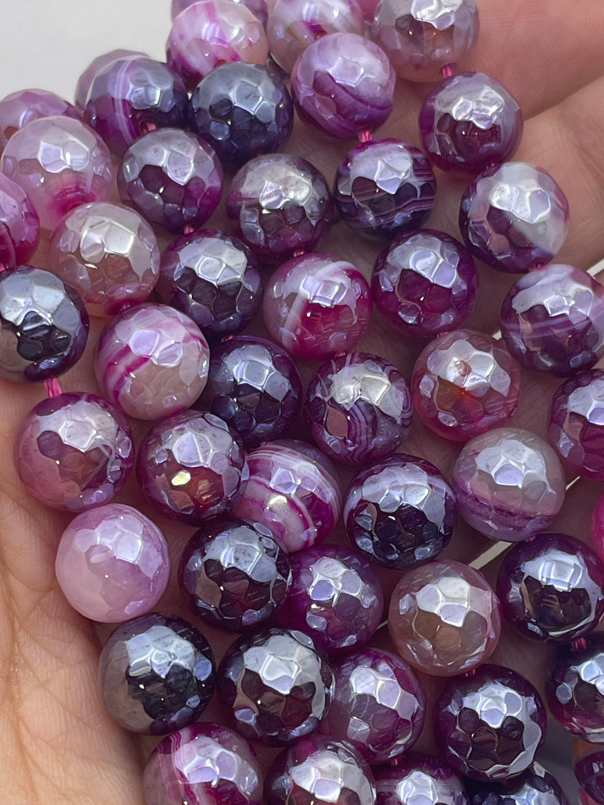 Faceted round agate gemstone beads in shades of purple, pink, and white, held in a hand.