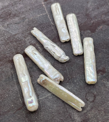Seven natural baroque freshwater pearl beads with an iridescent finish, displayed on a dark textured slate surface.