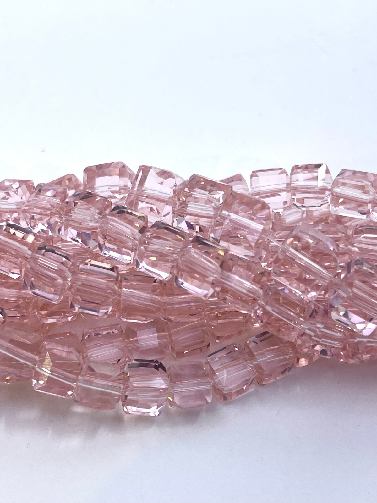 A close-up of a strand of faceted, cube pink glass beads on a plain white background.