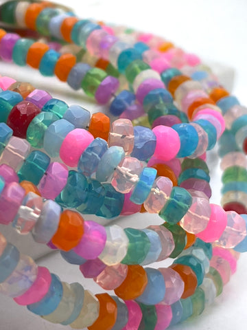 Close-up of multiple strands of faceted ethopian opal beads in assorted pastel and bright colors including pink, blue, teal, orange, purple, green, and clear tones, arranged on a white surface.