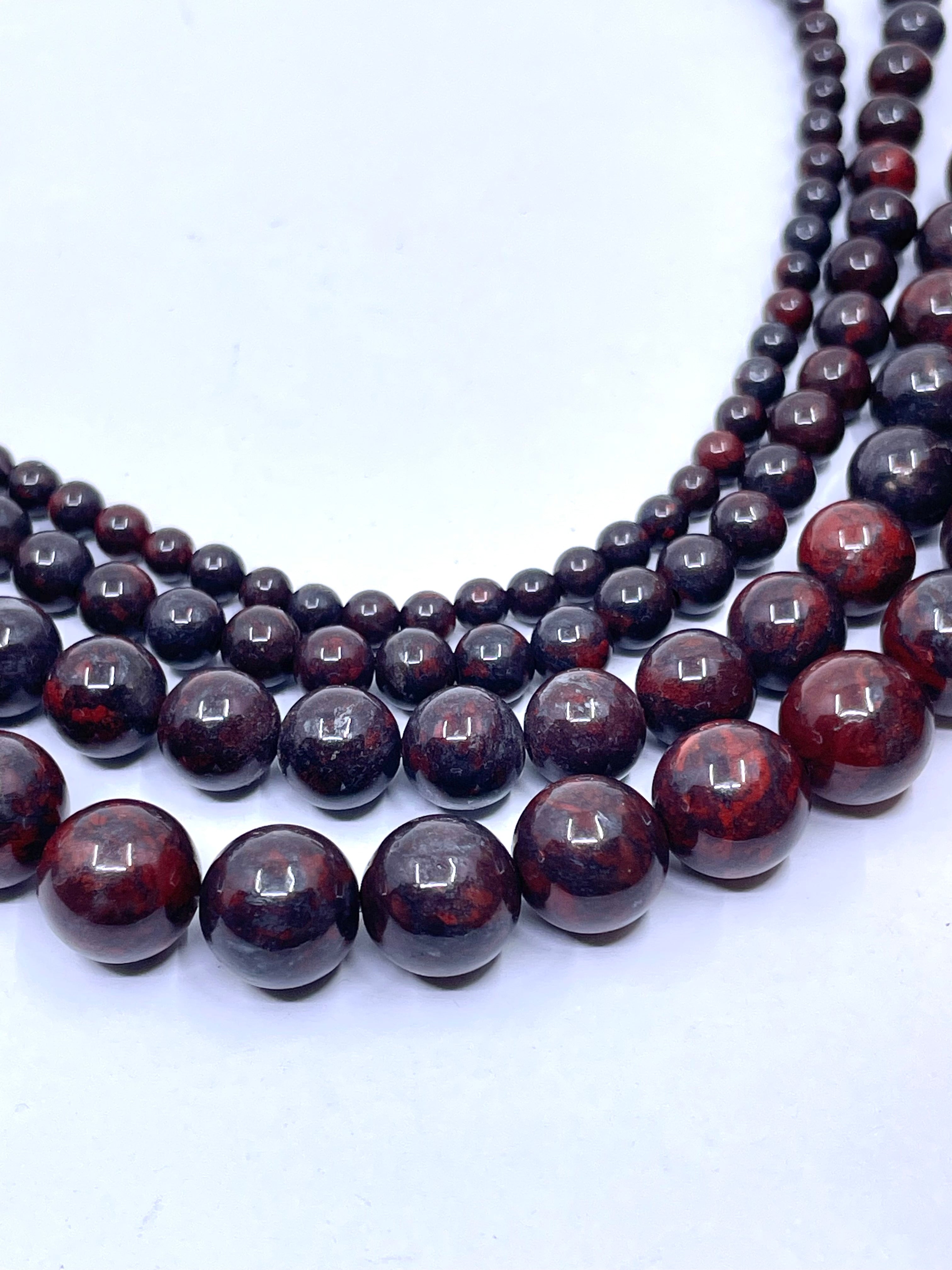 Multiple strands of polished dark reddish-brown brecciated jasper beads arranged in concentric curves on a plain white background.