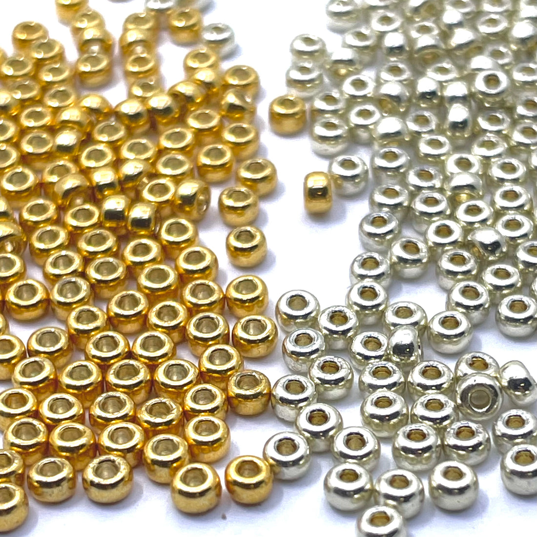 Small metallic look glass seed beads in two finishes: shiny gold beads on the left and silver beads on the right, scattered on a plain white background.