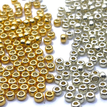 Small metallic look glass seed beads in two finishes: shiny gold beads on the left and silver beads on the right, scattered on a plain white background.