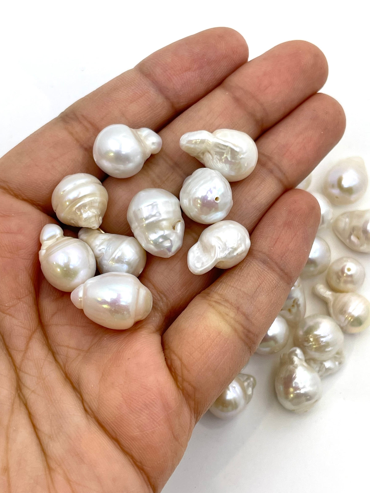A hand holding several irregular white baroque pearls, with more pearls scattered on a white background.