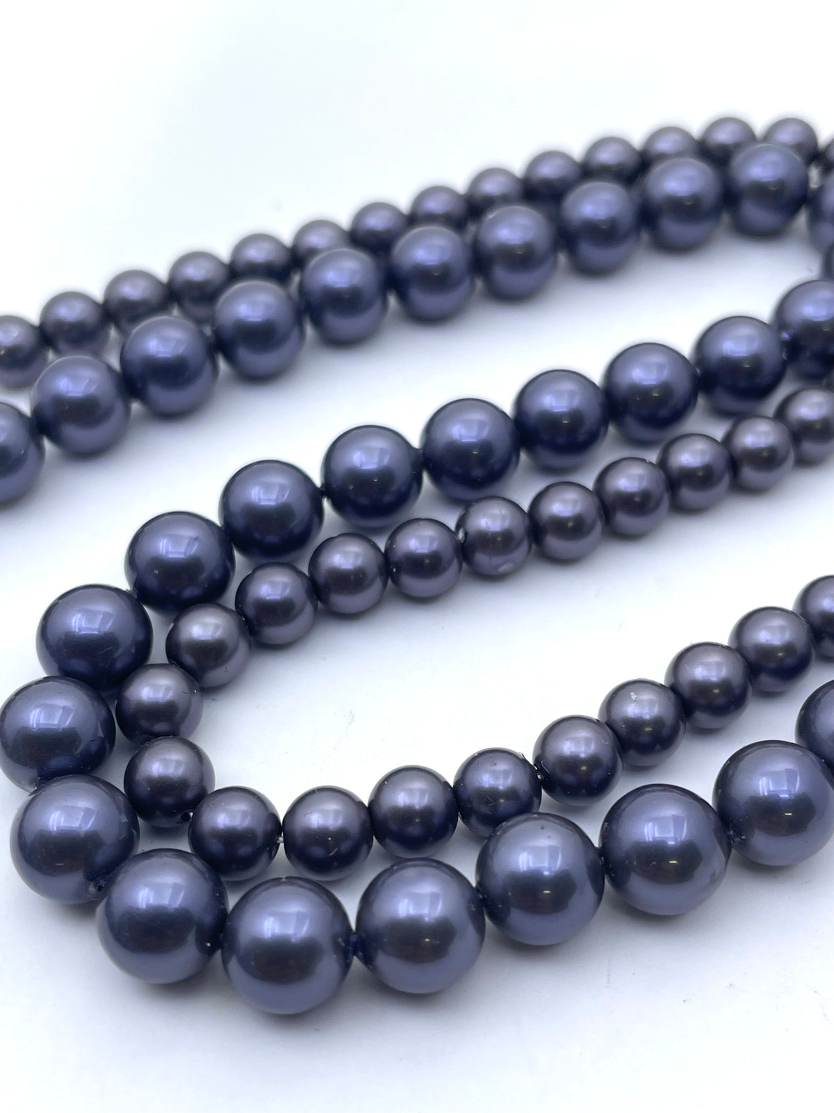A close-up of a multi-strand shell pearl beads with dark navy blue, lustrous round beads on a plain white background.