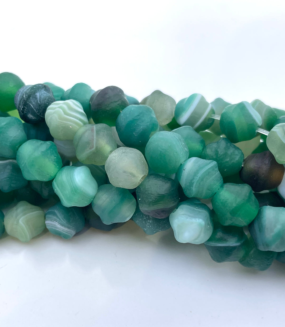 Green agate beads with natural marbled patterns in various shades of emerald, teal, and mint, arranged in a curved row on a white background.