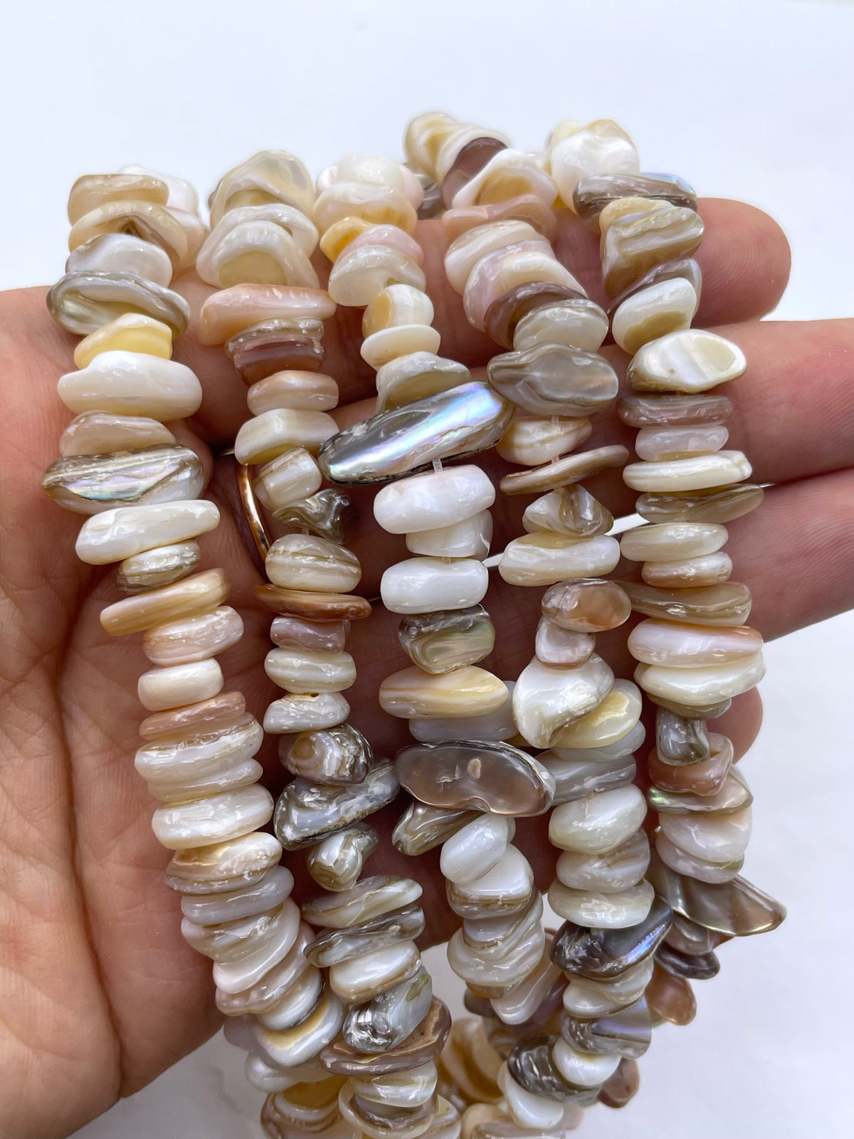 A hand holding a bundle of multi-strand  irregular, polished shell pieces in natural shades of cream, beige, brown, and white.