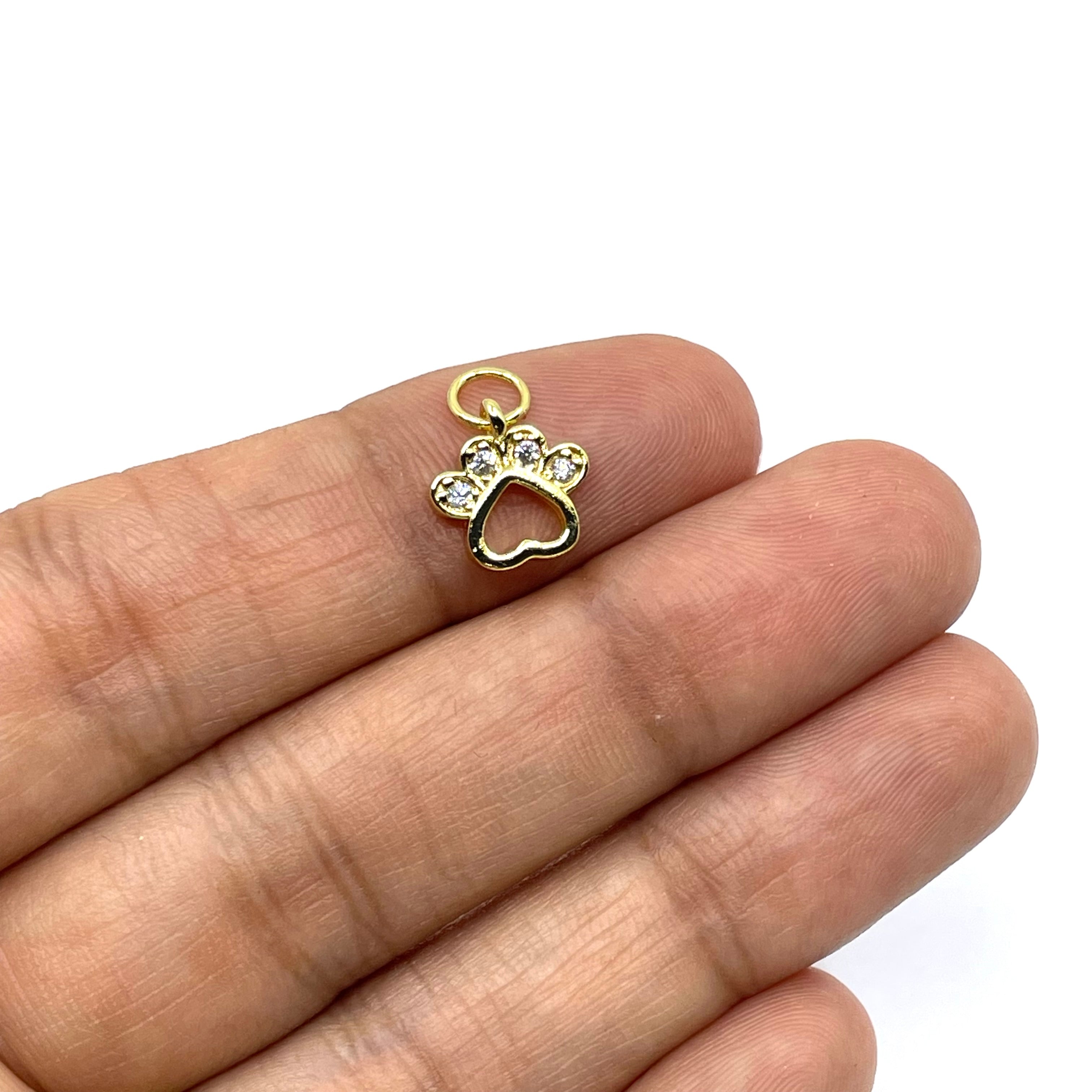 A small gold paw-shaped charm with clear rhinestones and a heart-shaped cutout, resting on a person's fingers against a white background.