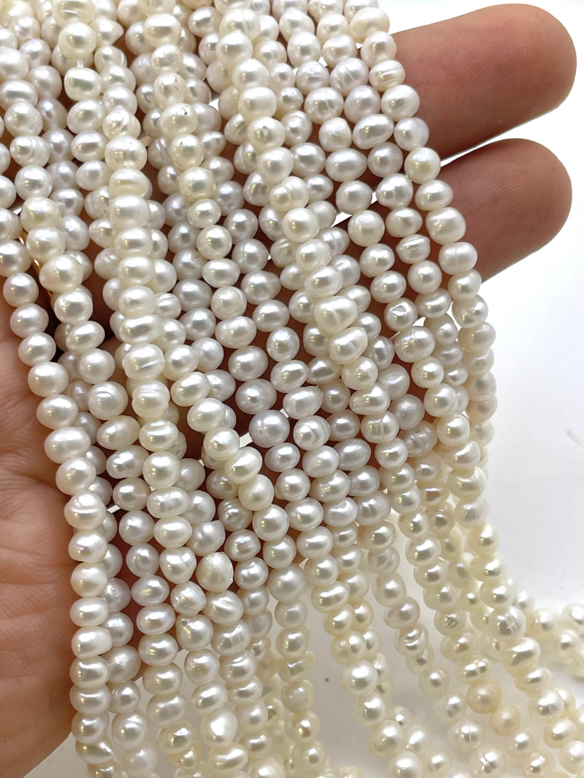 Multiple strands of white freshwater pearl beads held in a hand, showing their lustrous, glossy finish and irregular natural shapes.