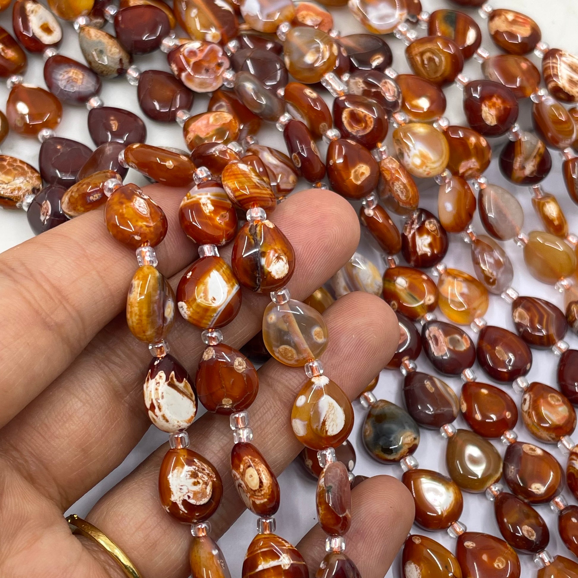 A close-up of a hand holding strands of polished brown and amber terracotta beads with silver spacer beads, with more of the same beads scattered in the background.