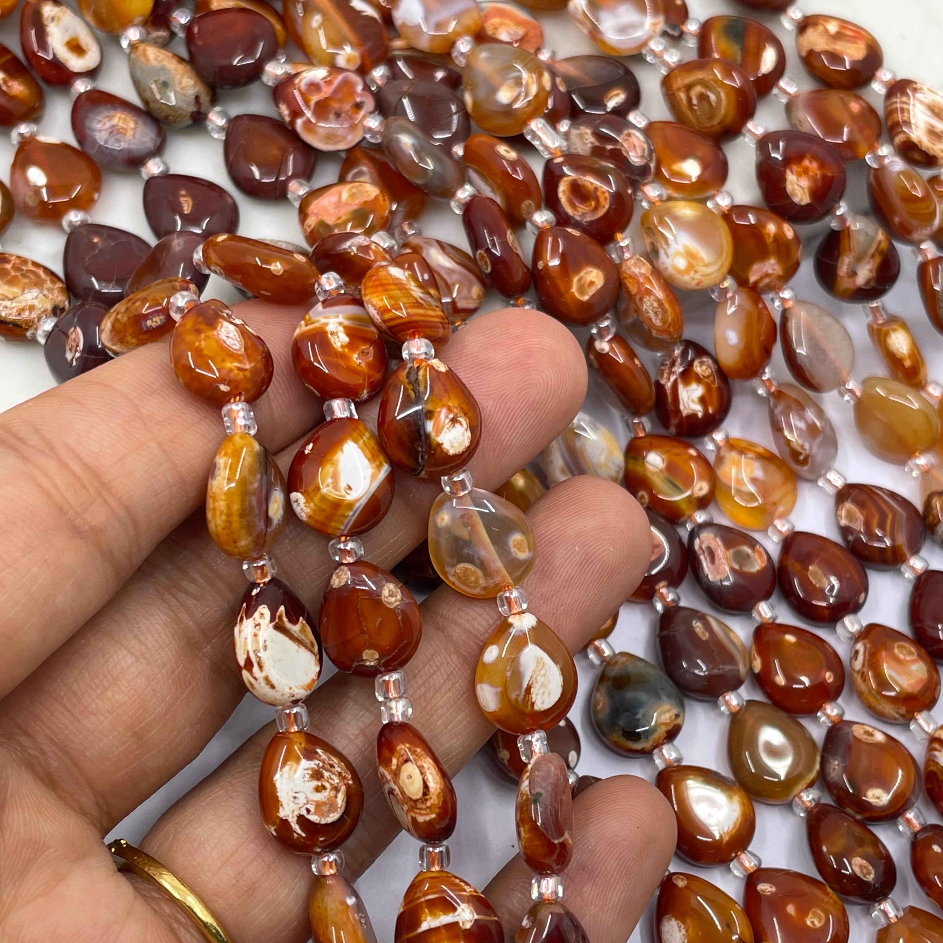 A close-up of a hand holding strands of polished brown and amber terracotta beads with silver spacer beads, with more of the same beads scattered in the background.