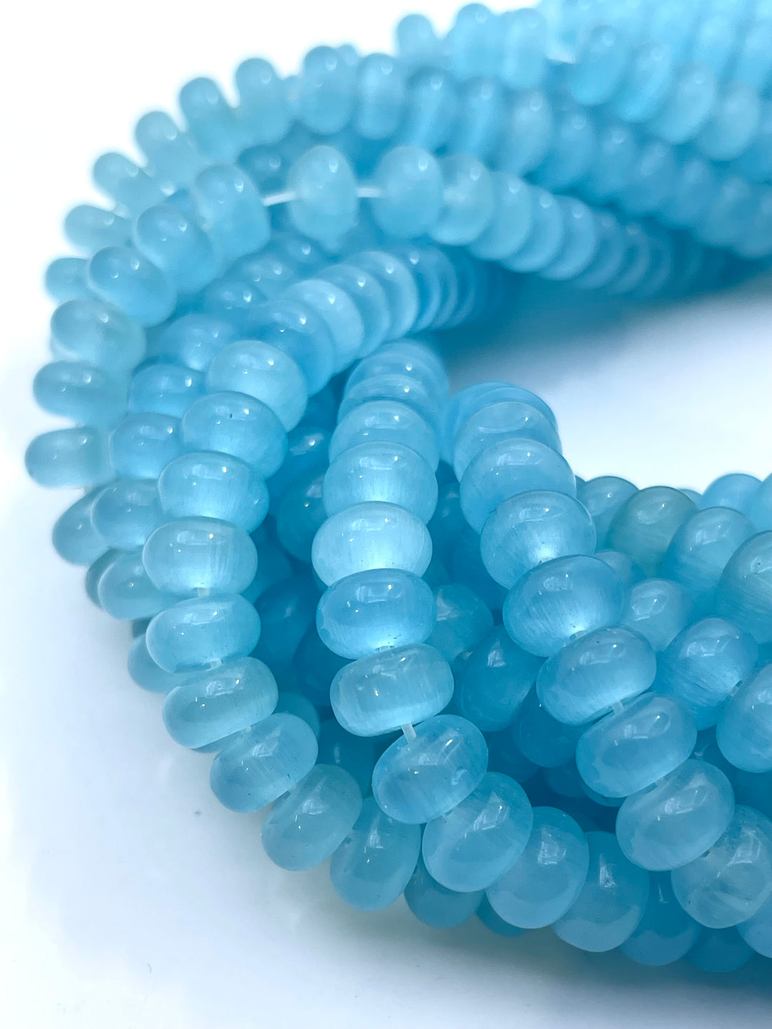 Light blue cats eye translucent donut gemstone beads strung on cords, held in a hand against a white background.