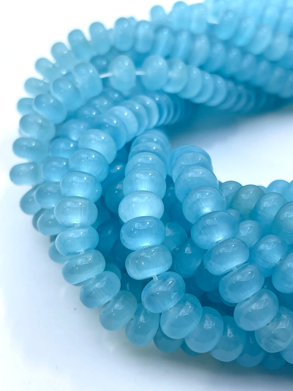 Light blue cats eye translucent oval beads strung on cords, arranged in overlapping loops on a white background.