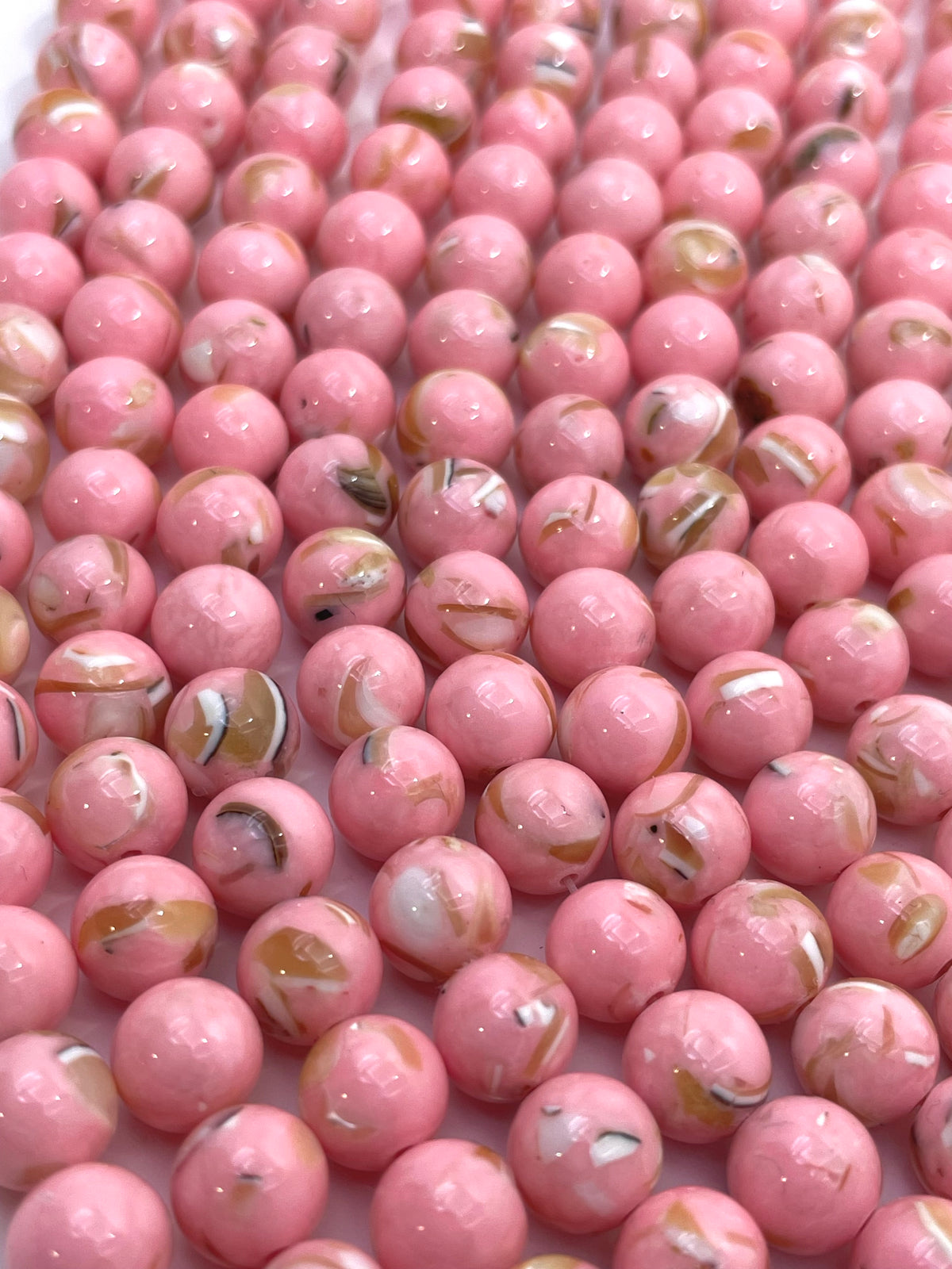 A close-up of many glossy pink round mop beads with small white, tan, and dark flecks throughout, filling the frame.