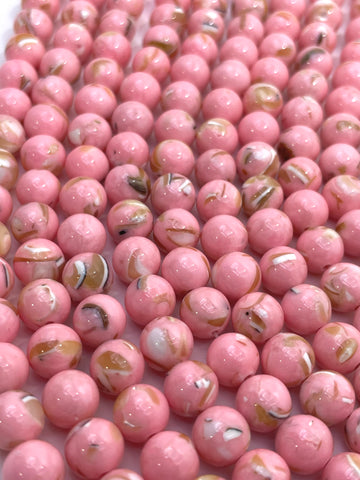 A close-up of many glossy pink round mop beads with small white, tan, and dark flecks throughout, filling the frame.