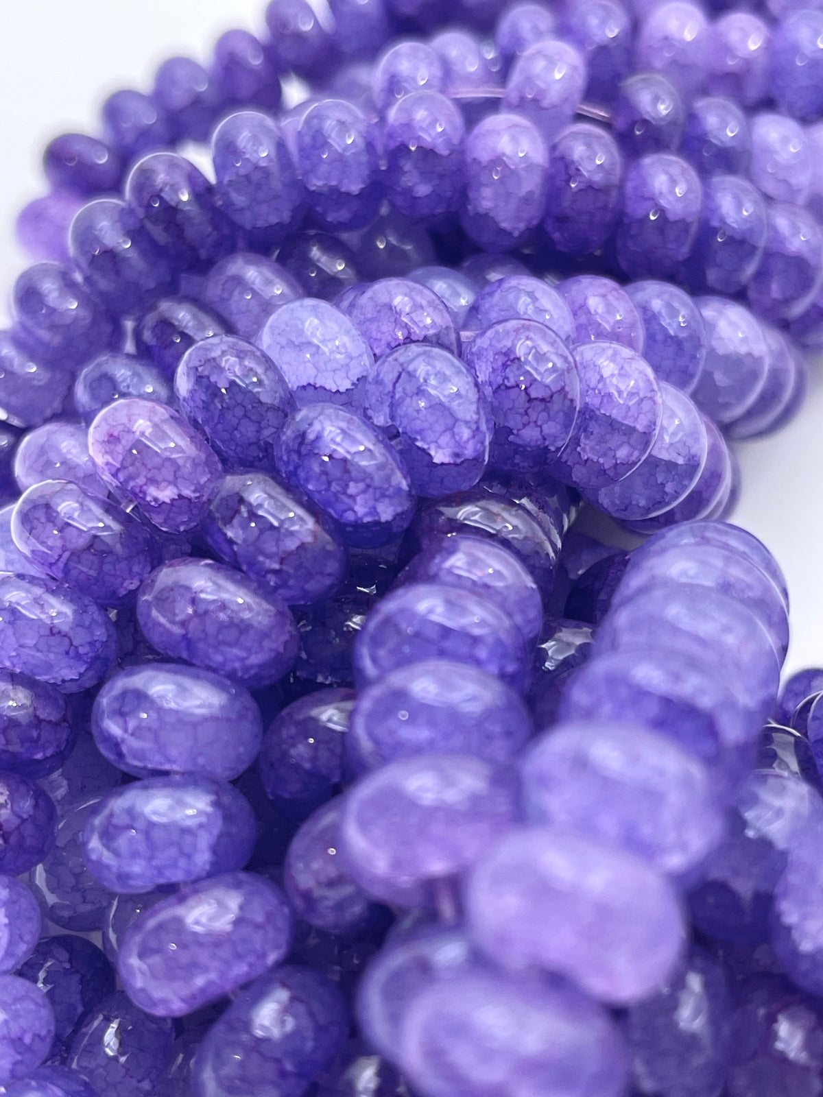Close-up of purple smooth donut glass beads, arranged in strands against a white background.