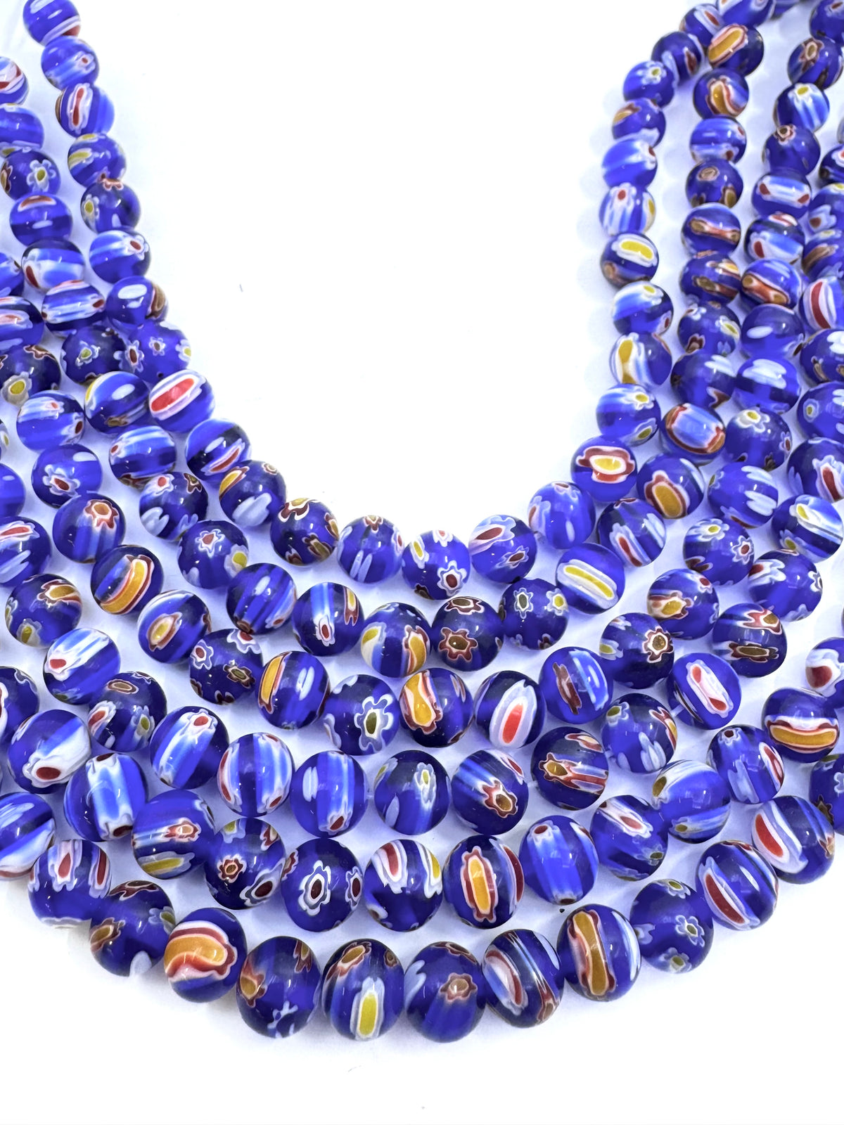 Multiple strands of round glass beads in deep cobalt blue, featuring swirls of white, orange, and yellow, arranged on a plain white background.