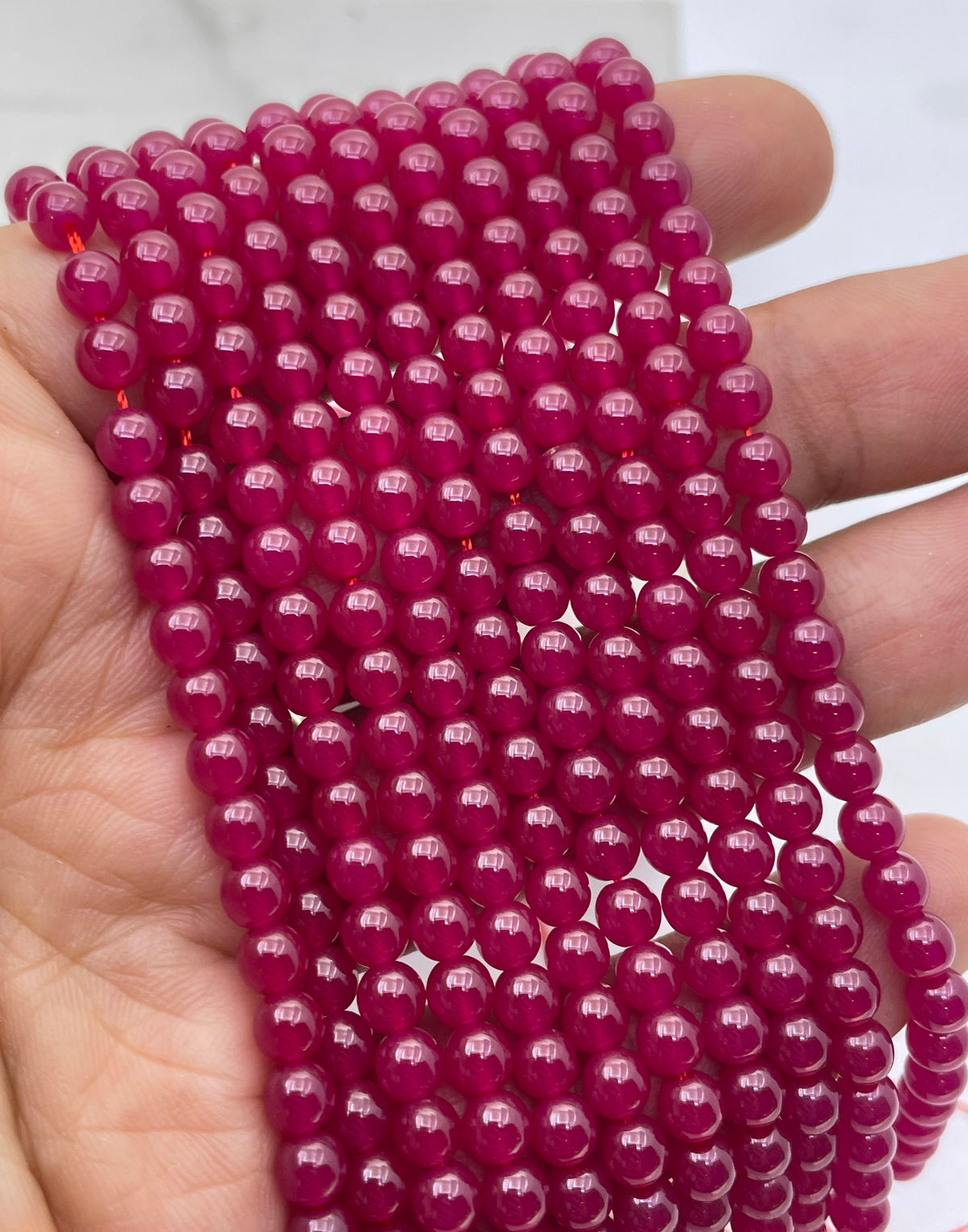 A close-up of a hand holding multiple strands of ruby glossy, magenta-pink beads.