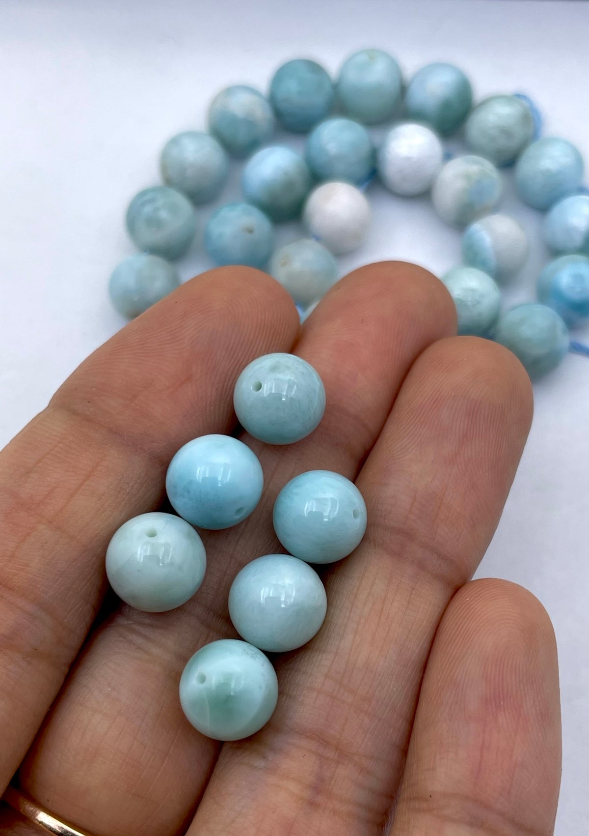 Light blue larimar round beads held in a person's hand, with more of the same beads blurred in the background.