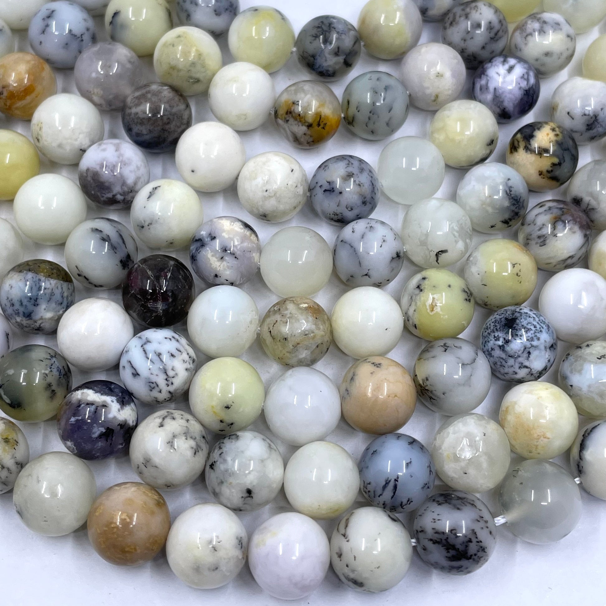Multiple strands of polished round dendritic opal beads in a marbled pattern of white, gray, beige, brown, and black, arranged on a plain white background.
