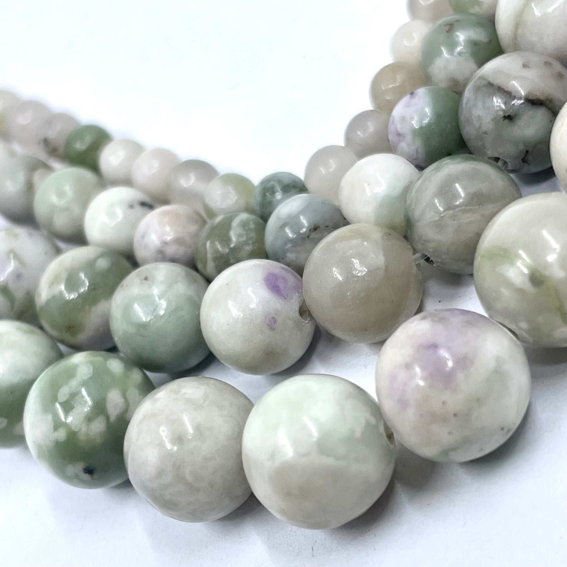 Close-up of polished round peace jade gemstone beads in pale green, white, and gray marbled tones, arranged on a white background.