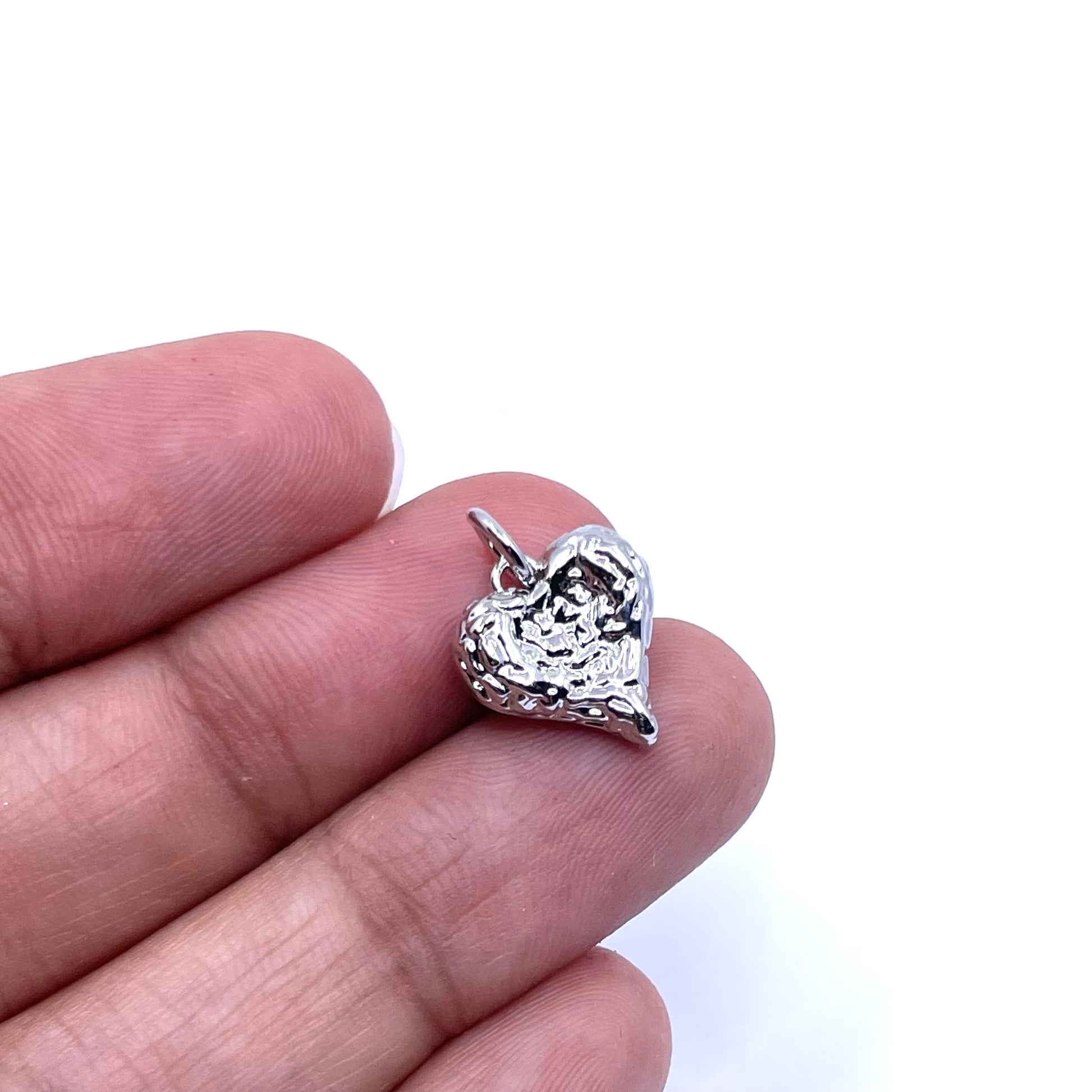 A small textured silver heart charm held between two fingers against a plain white background.