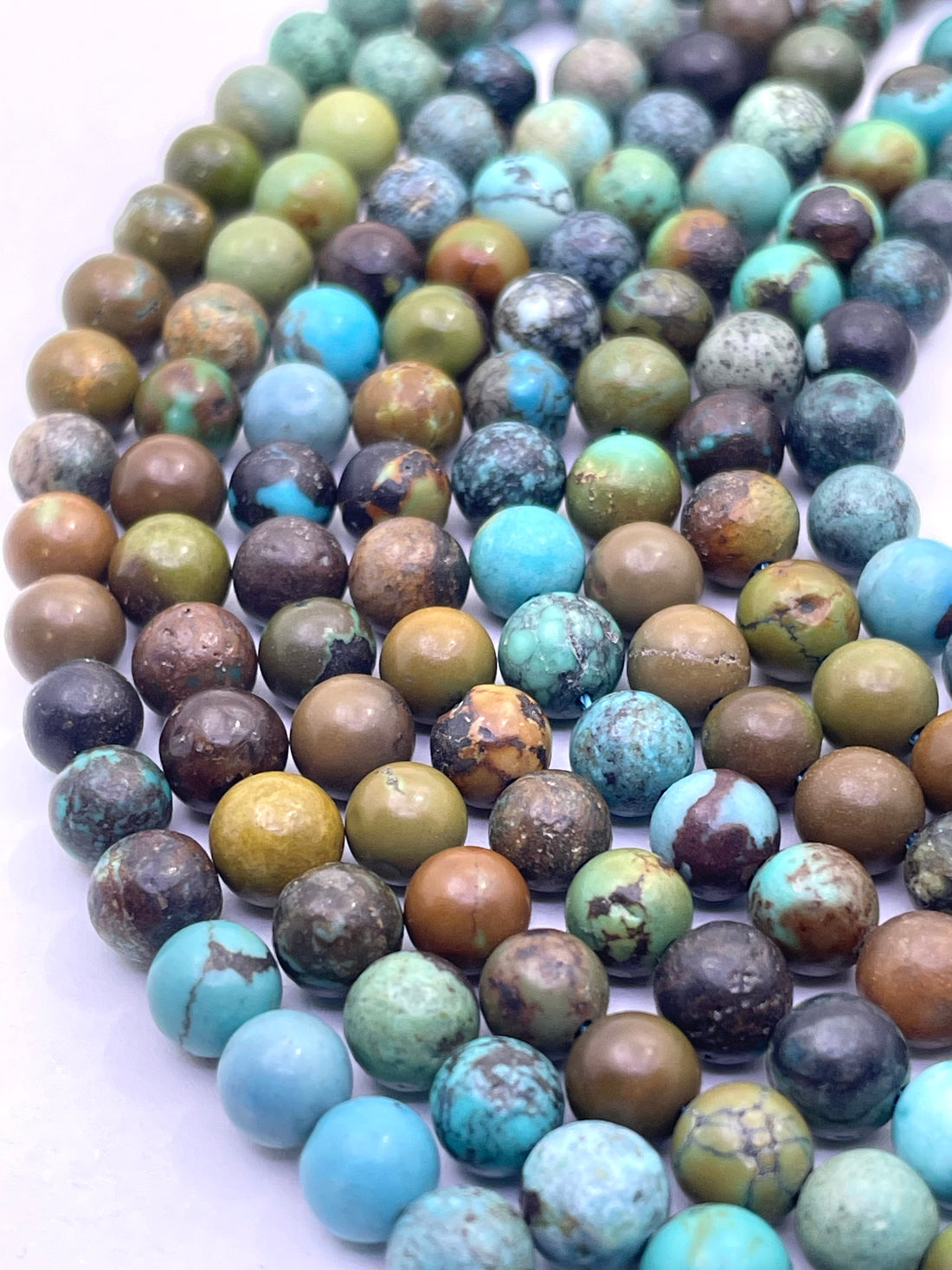 A close-up of a hand holding multiple strands of round turquoise stone beads in various earthy green, brown, blue, and turquoise colors.