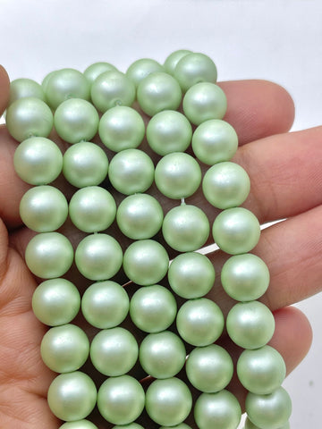 A close-up of a hand holding a strand of light green, pearl round beads against a plain white background.