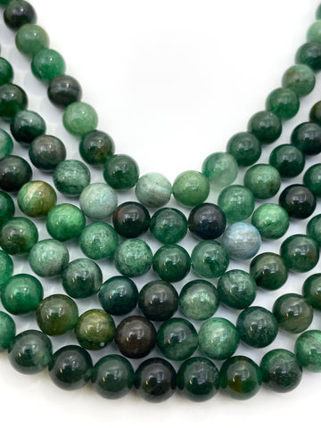 Multiple strands of polished round green lepidolite gemstone beads, varying from light forest green to dark emerald with natural inclusions, arranged on a plain white background.