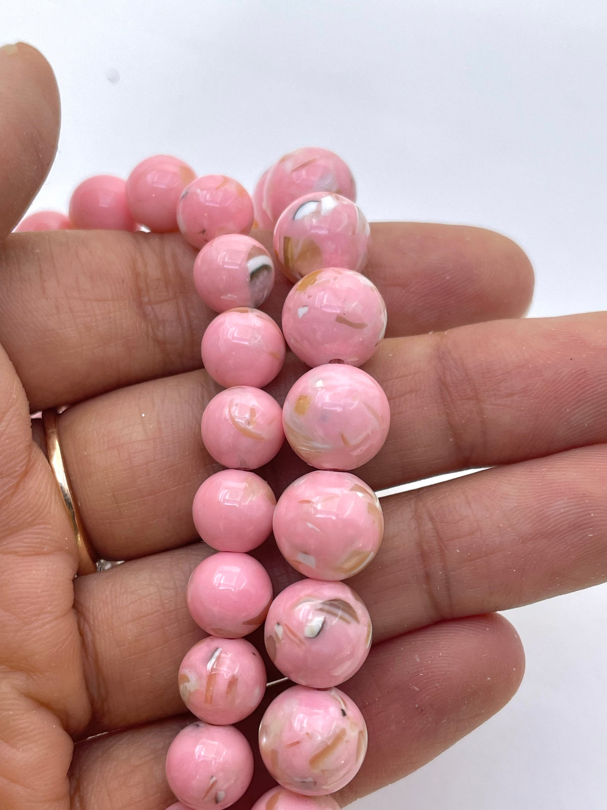 A close-up of a hand holding two strands of pink mop beads.
