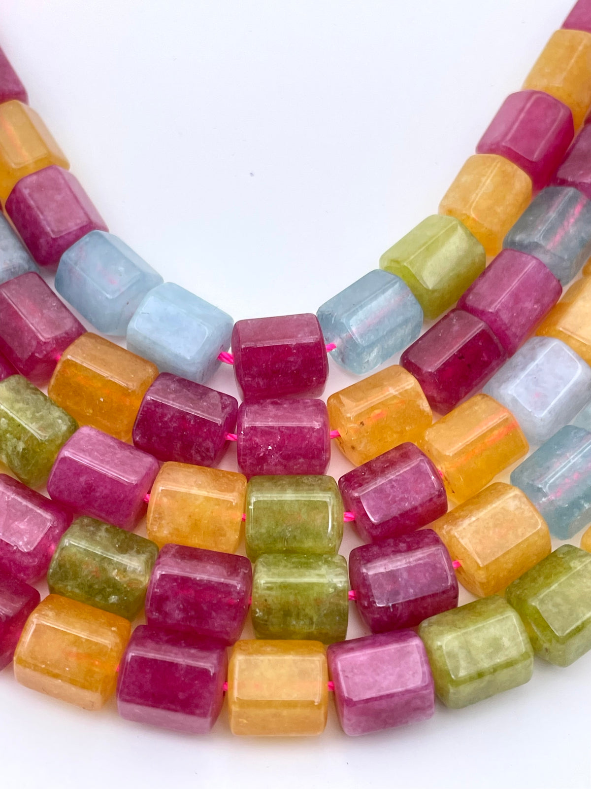 A close-up of a multi-strand mix jade beads featuring faceted, cube-shaped gemstone beads in assorted pastel and bright colors including pink, orange, yellow, green, and light blue, arranged in a U-shape on a plain white background.